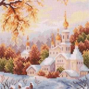 Può includere: Paesaggio a punto croce raffigurante un villaggio innevato con una chiesa. La scena presenta edifici con tetti bianchi e cupole dorate, circondati da alberi autunnali nei toni dell'arancione e del marrone. Un sentiero attraversa la neve.