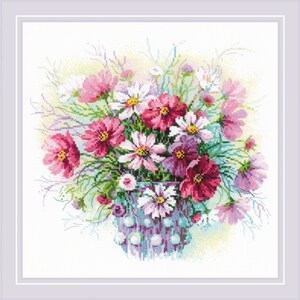 Può includere: Immagine a punto croce di una composizione floreale. Il bouquet comprende fiori di cosmea rosa, bianchi e bordeaux con centri gialli e foglie verdi, disposti in un vaso blu e bianco. L'opera è incorniciata in un bordo bianco.