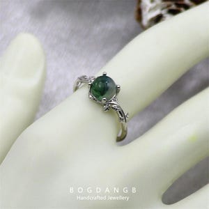 May include: A silver ring with a green agate gemstone and a leafy design. The ring is on a mannequin hand.
