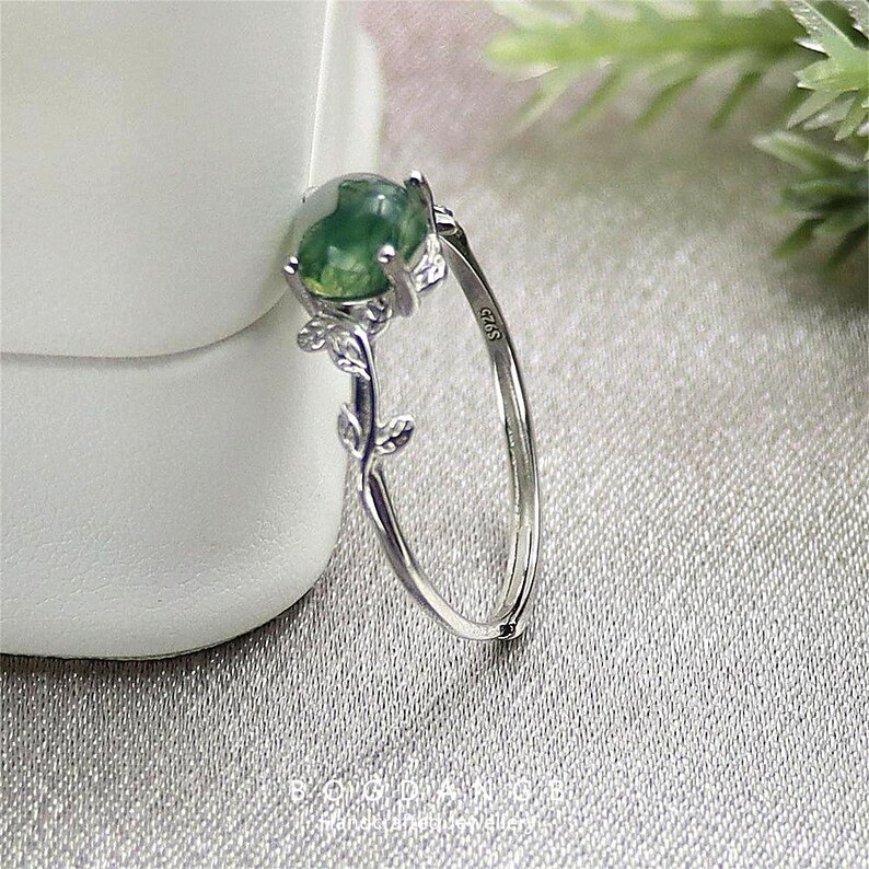 May include: A silver ring with a green agate stone set in a floral design. The ring is marked with the number "925" on the band.