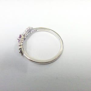 May include: A silver ring with a crown design, featuring a central purple gemstone and smaller accent stones. The ring is marked with "S925 ALE 56". The ring is set against a white background.