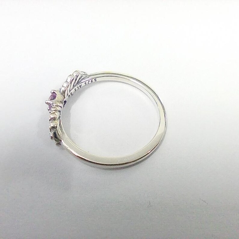 May include: A silver ring with a crown design, featuring a central purple gemstone and smaller accent stones. The ring is marked with "S925 ALE 56". The ring is set against a white background.