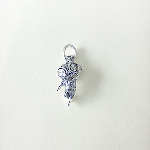 May include: A silver pendant in the form of a stylised insect. The pendant features large, round eyes with clear stones and is detailed with smaller stones. It has a loop at the top for a chain, suitable for jewellery.