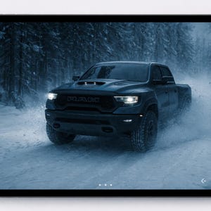 Puede incluir: Una camioneta gris oscuro, la RAM TRX, se muestra conduciendo por un bosque nevado. La camioneta levanta nieve mientras avanza. Los faros están encendidos y el logotipo de RAM es visible en la parte delantera.