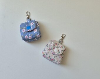 Può includere: Due piccole custodie quadrate in tessuto con motivi floreali e chiusure a scatto. Una è azzurra con fiori rosa, l'altra è bianco sporco con fiori rosa e verdi. Ognuna ha una chiusura in metallo color argento.