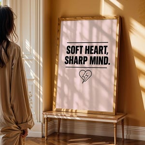 May include: A framed print with a pink background and black text that reads "Soft Heart, Sharp Mind." A stylized heart with a lightning bolt inside is below the text.