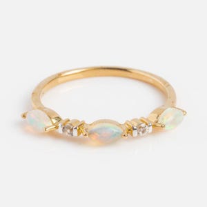 Può includere: Un anello d'oro con dettagli di opale e diamanti. Gli opali ovali sono disposti in fila, con piccoli diamanti intercalati. L'anello presenta un design delicato ed elegante.
