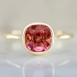 Hot Honey Pink-Peach Tourmaline Ring featuring a 1.81 carat cushion cut lab-created tourmaline set in 14k yellow gold. The gemstone glows with vibrant hues of pink, peach, orange, and red that shift in different lighting. A rounded bezel setting keeps the design sleek and modern, while the slim 1.71 mm band makes it perfect for stacking with other rings. A versatile and radiant gemstone ring that blends everyday luxury with a bold pop of color.