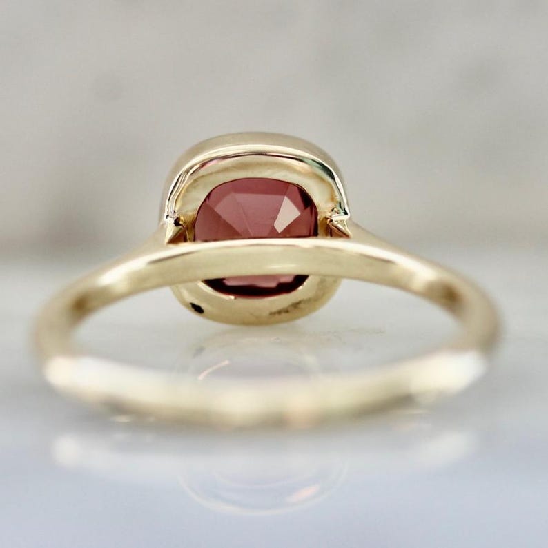 Hot Honey Pink-Peach Tourmaline Ring featuring a 1.81 carat cushion cut lab-created tourmaline set in 14k yellow gold. The gemstone glows with vibrant hues of pink, peach, orange, and red that shift in different lighting. A rounded bezel setting keeps the design sleek and modern, while the slim 1.71 mm band makes it perfect for stacking with other rings. A versatile and radiant gemstone ring that blends everyday luxury with a bold pop of color.