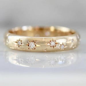 May include: A gold band ring featuring a delicate design of small diamonds set in star shapes. The ring is a simple and elegant piece of jewellery.