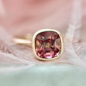 Hot Honey Pink-Peach Tourmaline Ring featuring a 1.81 carat cushion cut lab-created tourmaline set in 14k yellow gold. The gemstone glows with vibrant hues of pink, peach, orange, and red that shift in different lighting. A rounded bezel setting keeps the design sleek and modern, while the slim 1.71 mm band makes it perfect for stacking with other rings. A versatile and radiant gemstone ring that blends everyday luxury with a bold pop of color.