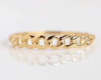 Könnte beinhalten: Ein goldfarbener Kettenring. Der Ring hat ein durchgehendes Kettenglied-Design. Der Ring wird auf einer reflektierenden Oberfläche gezeigt, die das Design des Rings widerspiegelt. Der Ring ist ein schlichtes, elegantes Schmuckstück.