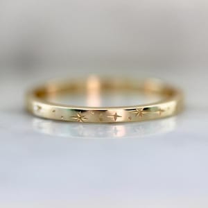 Puede incluir: Un anillo de oro con un diseño celestial. El anillo presenta una serie de estrellas y puntos grabados alrededor de la banda. El anillo tiene un acabado pulido y refleja la luz, creando un brillo sutil. Una joya delicada.