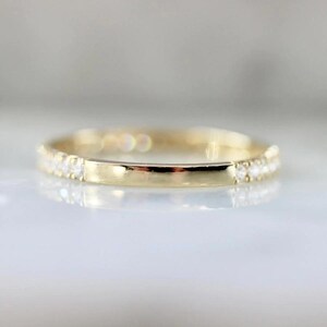 Puede incluir: Un anillo de banda de oro con una fila de peque&ntilde;as piedras preciosas transparentes engastadas en la parte superior y una banda de oro lisa y pulida. El anillo est&aacute; sobre un fondo suave y borroso.