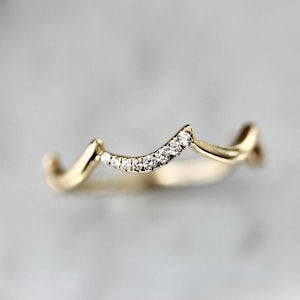May include: A delicate gold band ring with a wavy design and a row of small diamonds.
