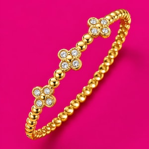 May include: A gold-toned beaded bracelet featuring three evenly spaced four-leaf clover motifs. Each clover is crafted from polished gold metal and set with four small, clear, round-cut sparkling stones at the centre of each petal.
