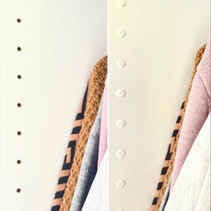 Może przedstawiać: Biała ściana z rzędem otworów po lewej stronie i rzędem białych kropek po prawej stronie. Na prawej stronie ściany wisi stos swetrów w różnych kolorach i wzorach.