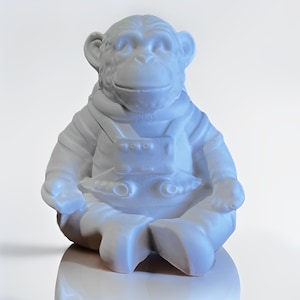 May include: A white ceramic monkey figurine in a seated position, wearing a spacesuit. The monkey is depicted with its legs crossed and arms resting on its lap. The figurine has a smooth, matte finish and is set against a white background.