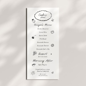 May include: A white rectangular menu card with black hand-drawn text and illustrations. The text reads Cade's place, Tonight's Menu, Chicken Shawarma, Coconut Rice, Quinoa Salad, Pita Bread, Homemade Hummus, Homemade Tzatziki, Homemade Garlic Dip, Dessert, Jeni's Ice Cream, Morning After, Apple Muffins, Congratulations on your beautiful baby boy!, We love you!, The Smith Family.