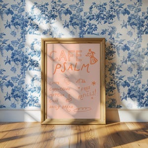 Puede incluir: Un letrero enmarcado con las palabras "CAFE PSALM" en escritura naranja. El letrero enumera bebidas de caf&eacute; y t&eacute;, y "FREE REFILLS!" est&aacute; escrito debajo. El fondo es de color rosa claro y el marco es de color marr&oacute;n claro. El fondo es un papel pintado floral azul y blanco.