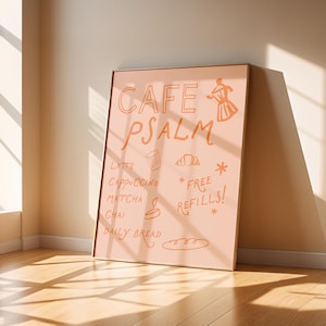 Puede incluir: Un p&oacute;ster enmarcado con las palabras "CAFE PSALM" en escritura naranja. El p&oacute;ster enumera bebidas de caf&eacute; y t&eacute;, y "FREE REFILLS!" tambi&eacute;n est&aacute; escrito en el p&oacute;ster. El p&oacute;ster est&aacute; apoyado contra una pared, con la luz del sol que atraviesa el suelo.