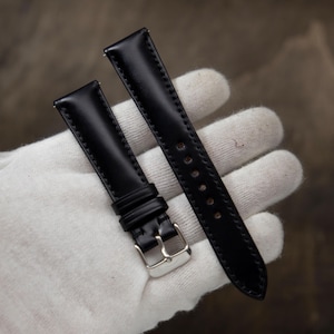 May include: A two-piece black watch strap with a smooth finish and tonal stitching. The strap features a silver-toned metal buckle and two sliding keepers on the shorter piece, while the longer piece contains a series of punched holes for adjustment.