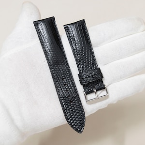May include: Two black watch straps with a textured, reptile-like pattern. One strap has a silver-colored buckle. The straps are displayed against a white background.