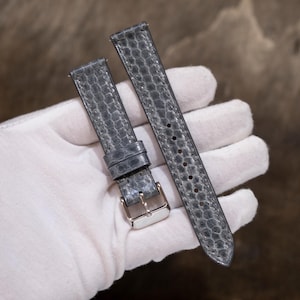 May include: A two-piece watch strap featuring a textured grey snakeskin pattern. The shorter piece includes a polished silver-tone metal buckle and a fixed loop, while the longer piece has a series of punched holes for adjustable sizing.