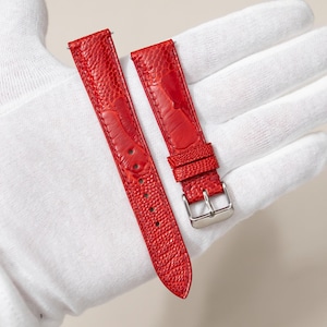 May include: Two vibrant red watch straps with a textured, ostrich-style leather finish. One strap has a silver-coloured buckle. The straps are shown on a white surface.