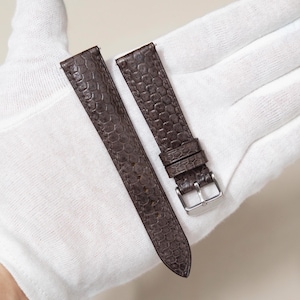 May include: Two brown leather watch straps with a textured, scale-like pattern. One strap has a silver-colored buckle. The straps are displayed on a white surface.