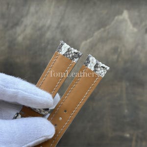 May include: A two-piece watch strap featuring a grey and white snakeskin pattern on the exterior and a smooth tan leather lining. The strap includes white contrast stitching along the edges and visible spring bars at the top attachment points.
