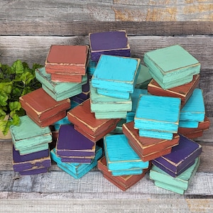 May include: A collection of wooden square blocks in various colors, including teal, turquoise, purple, green, and orange. The blocks are stacked and arranged in a random pattern.