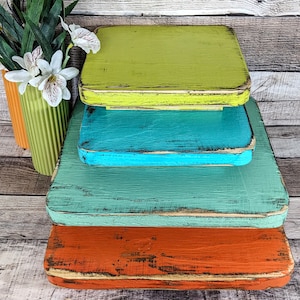 May include: Four wooden tiered trays in shades of green, blue, teal, and orange. The trays are stacked on top of each other and have a distressed, rustic look.