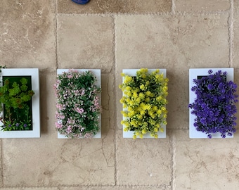 May include: Four white framed wall planters with different colored artificial plants. The plants are green, pink, yellow, and purple.