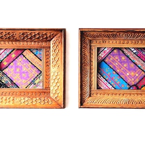 Pode incluir: Duas peças de arte de parede com moldura de madeira. Cada moldura tem detalhes entalhados intrincados e envolve um design têxtil colorido. Os têxteis apresentam uma mistura de padrões roxos, azuis, rosa e dourados, criando uma exibição vibrante e decorativa.