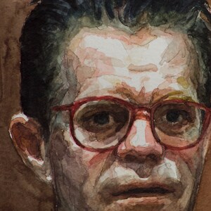 May include: A close-up portrait of a person with short dark hair wearing red-rimmed glasses. The person has a serious expression and is looking directly at the viewer.