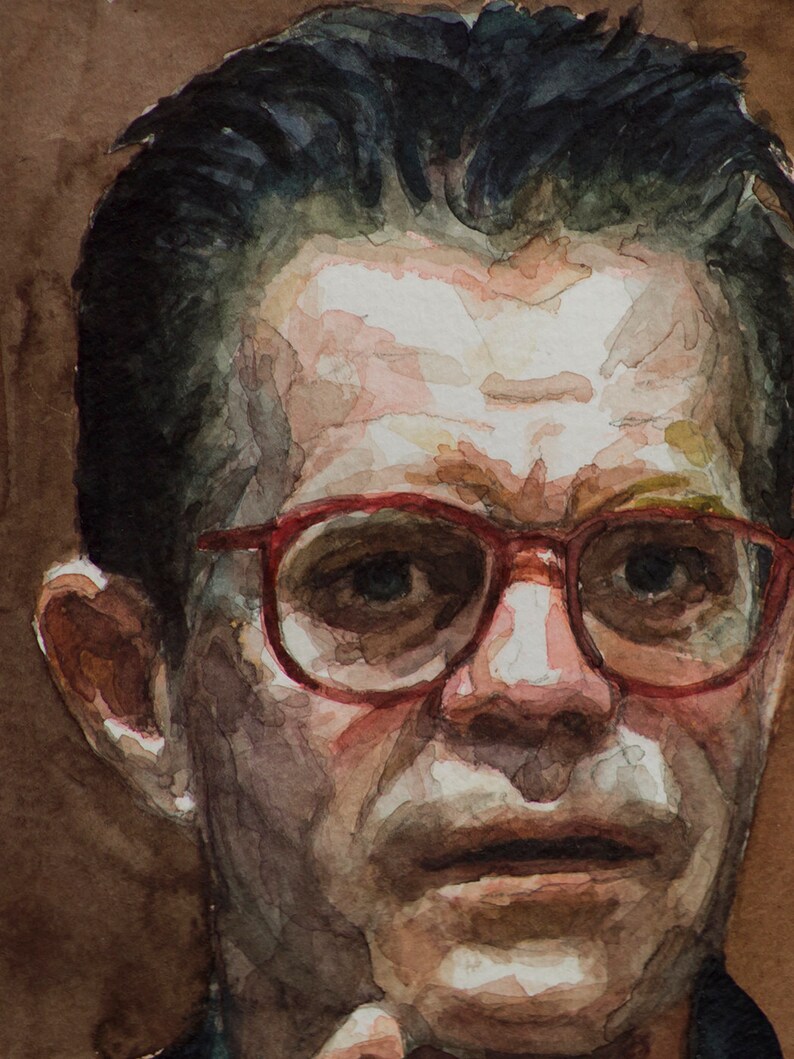 May include: A close-up portrait of a person with short dark hair wearing red-rimmed glasses. The person has a serious expression and is looking directly at the viewer.
