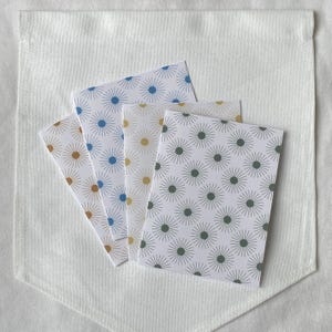 May include: Four small cards with a white background and a repeating pattern of radiating lines and circles in shades of blue, gold, and green. The cards are arranged in a fan shape against a white pocket.