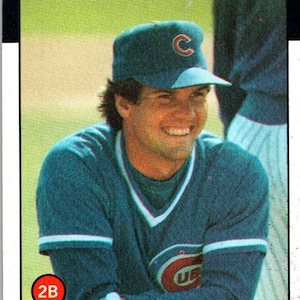 May include: Baseball card featuring Ryno Sandberg of the Chicago Cubs. The card has a red "CUBS" header and the player's name at the bottom. Sandberg is wearing a teal uniform and cap with the Cubs logo.