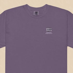 May include: Purple t-shirt with a graphic of teeth and the text "RADIATE POSITIVITY" on the front.