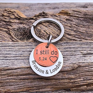May include: A silver keychain with a copper penny attached. The penny has the words "I still do" and the date "5.24" engraved on it. The keychain also has a silver disc with the words "Bronson & London" engraved on it.
