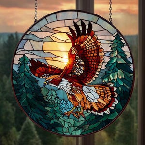 May include: Round stained glass window featuring a hawk in flight against a sunset backdrop. The hawk has brown, orange, and white feathers, with a detailed wing design. Green trees and blue sky complete the nature scene. The window is framed in a dark brown border.