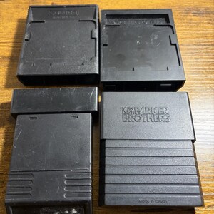 Puede incluir: Cuatro cartuchos de videojuegos de plástico negro dispuestos en una cuadrícula de dos por dos. El cartucho superior izquierdo está marcado como Coleco. El superior derecho dice Parker Brothers. El inferior derecho tiene el logo de Parker Brothers.