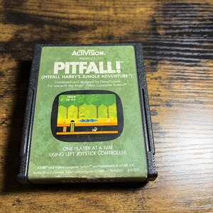 May include: A black Atari 2600 video game cartridge for the game Pitfall! featuring a green label with the Activision logo, game title, and a screenshot of the jungle adventure gameplay. The text includes instructions for one player and controller use.