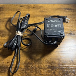 May include: A black power supply adapter with a long cord and a two-prong plug. The rectangular unit features printed text including 'POWER SUPPLY', 'PART NUMBER: C017945', 'INPUT 120V 60HZ 50W', 'OUTPUT 9V AC 31 VA', and 'CAUTION INDOOR USE ONLY'.