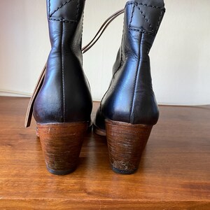 May include: Black leather ankle boots with wooden heels. The boots have a pull tab at the top and a stitched design on the back. The heels are approximately 3 inches tall.