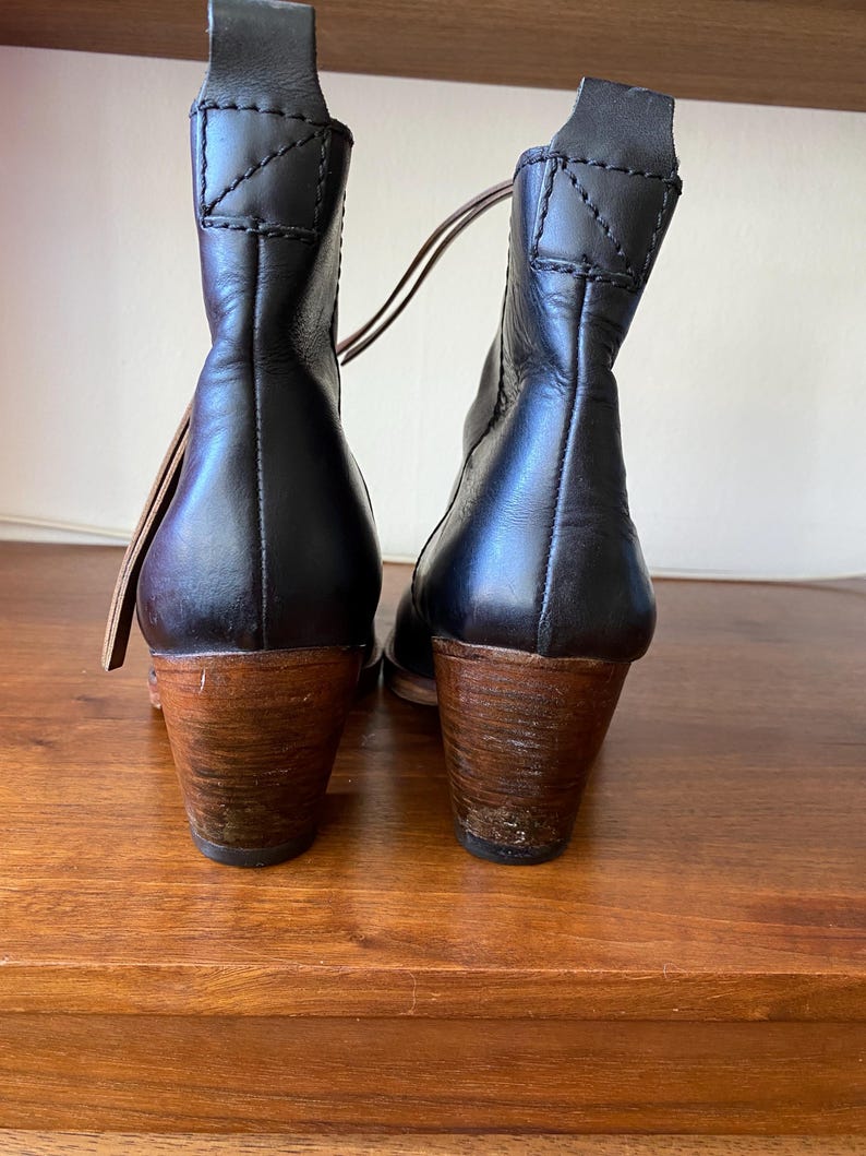 May include: Black leather ankle boots with wooden heels. The boots have a pull tab at the top and a stitched design on the back. The heels are approximately 3 inches tall.