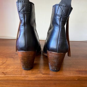 May include: A pair of black leather ankle boots with wooden heels. The boots have a pull tab at the back and a brown leather accent. The heels are approximately 3 inches tall.