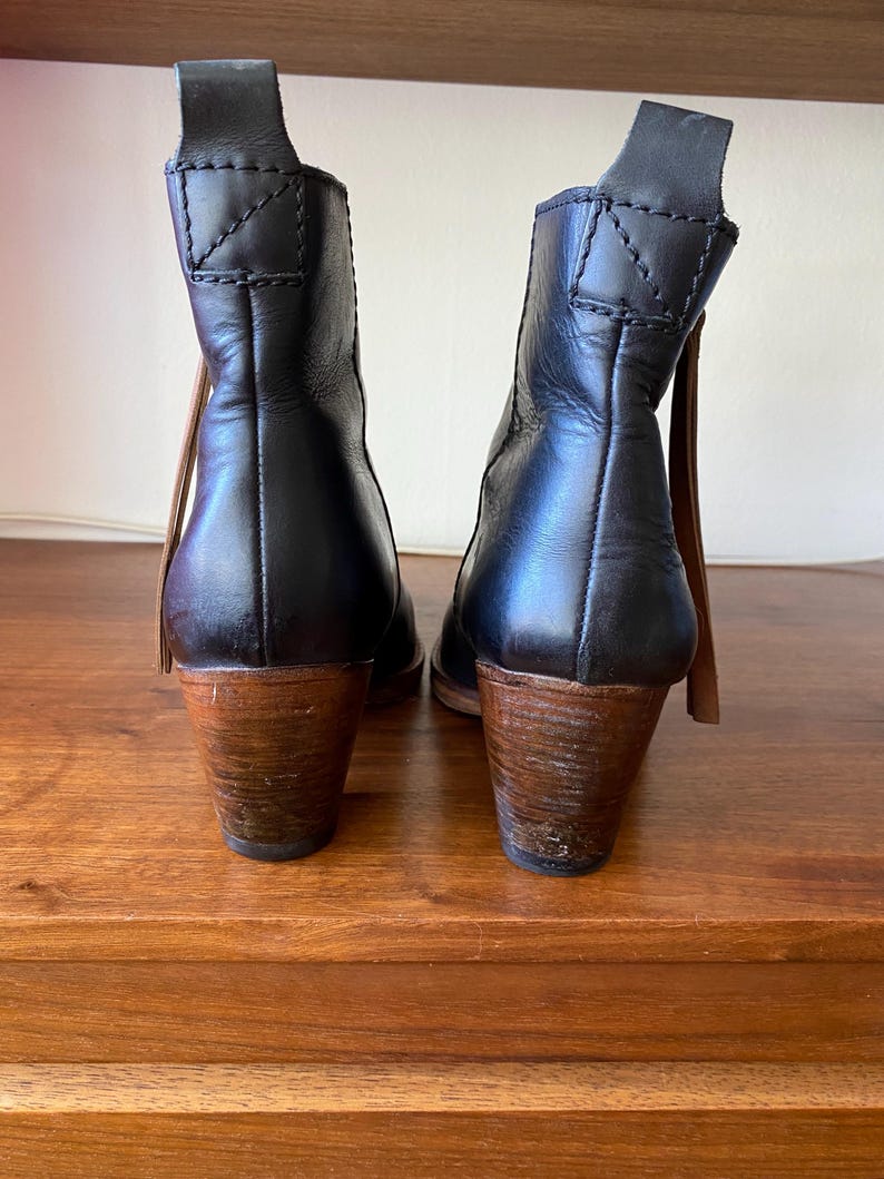May include: A pair of black leather ankle boots with wooden heels. The boots have a pull tab at the back and a brown leather accent. The heels are approximately 3 inches tall.