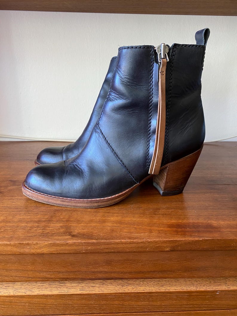 May include: Black leather ankle boots with a wooden heel and a side zipper. The boots have a rounded toe and a pull tab at the back. The heel is approximately 3 inches high.